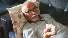 Senior man laying down on the sofa, watching tv and holding the remote control.