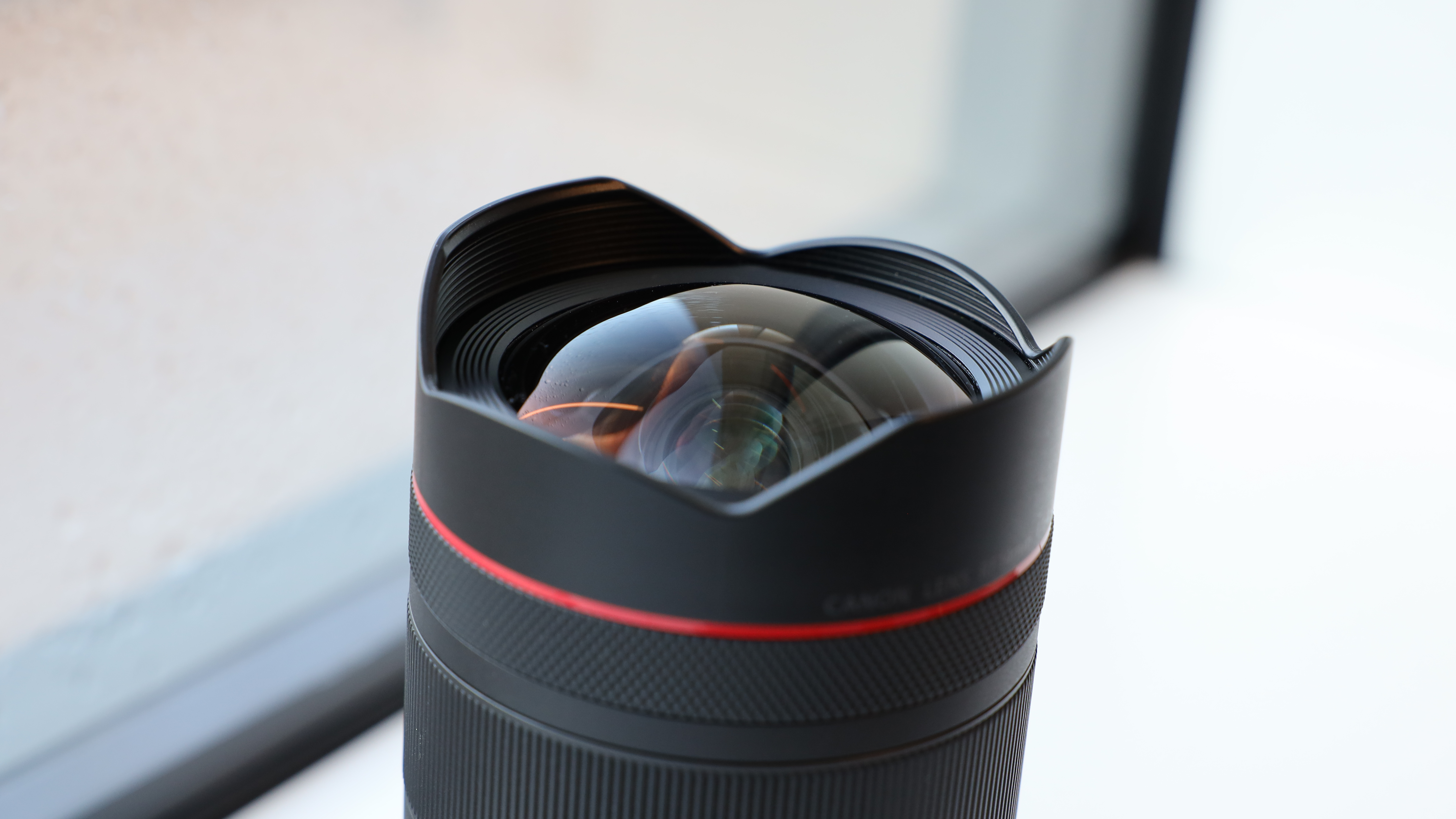 Close up of the front lens element on a Canon RF 14mm f/1.4L VCM lens on a windowsill