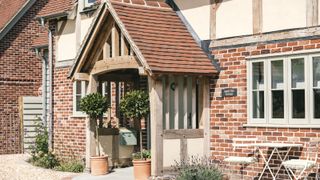 oak frame porch with tiled roof on oak and brick home with table and chairs to one side, plant pots to entrance