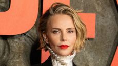 Image of Charlize Theron with blonde chin-length bob, wearing red lipstick and a white high-neck pleated shirt