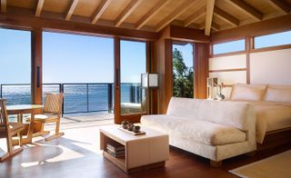 Interior view of a room at Nobu Ryokan, Malibu, US featuring a wooden interior, a light coloured bed, sofa and coffee table, a wooden table and wooden chairs. There is also a view of the sea