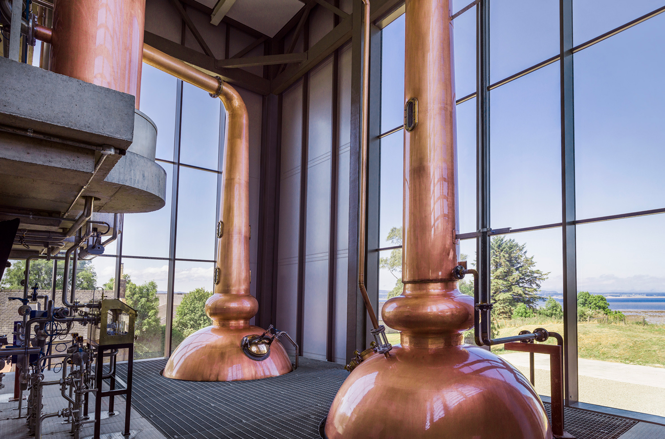 Whisky stills next to a full-length window with the sea in the background