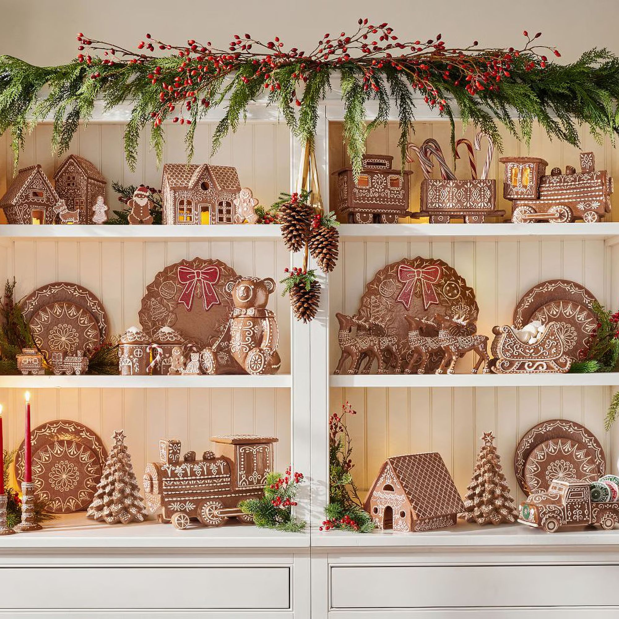 Pottery Barn&#039;s Christmas tableware with gingerbread designs displayed in a cabinet with a garland on top