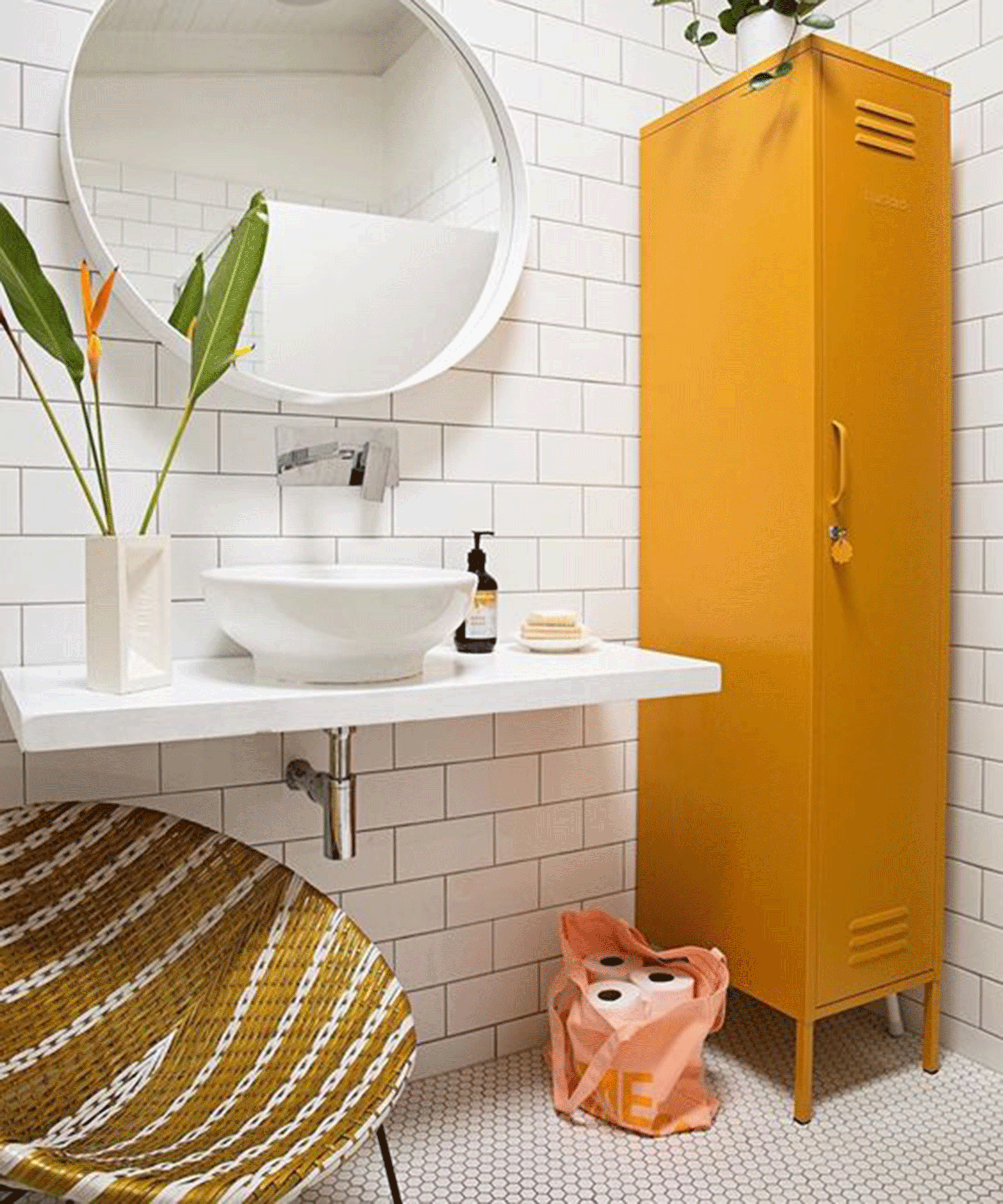 Bright yellow bathroom cabinet in white tiled bathroom with wall mirror and woven chair