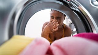 A woman looking into a washing machine at clothes while holding her nose