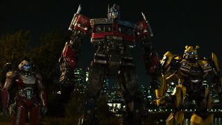 Optimus Prime stands with Arcee and Bumblebee in a night scene in Transformers: Rise of the Beasts.