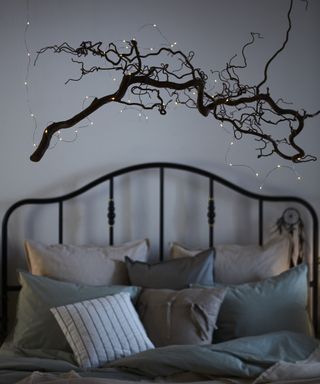 A grey bedroom with tree branch decor affixed to wall over bed with bedroom fairy lights
