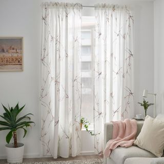 White curtains in white living room with wall art, houseplant and baby pink throw over neutral couch