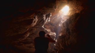 Person in a cave looking through a hole and seeing a bright sun