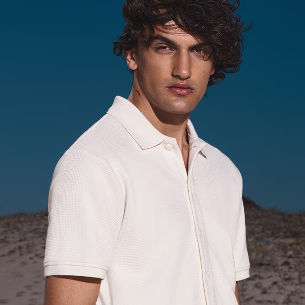 A man posing on a beach in a white polo shirt from George at Asda
