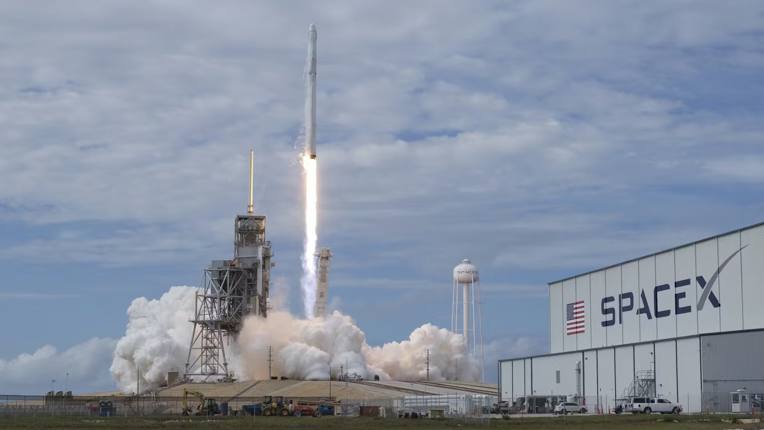 A rocket launching to space next to a SpaceX building.