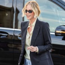 Charlize Theron wears pale blue satin shorts with a butter yellow blouse, a black blazer and silver strappy heels.