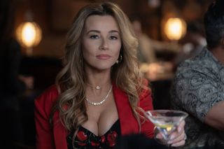 linda cardellini holds a martini at a bar and wears a red blazer and dress with cherries on it in no good deed