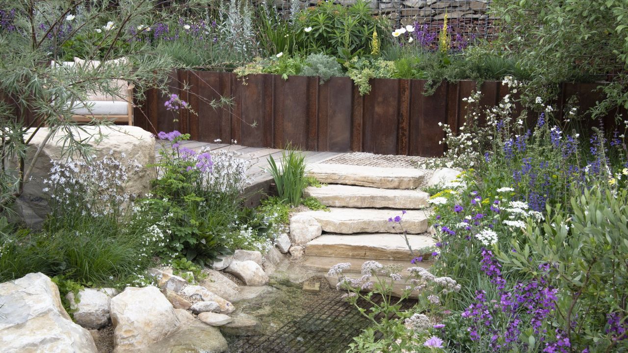 Flower beds surround a stone pathway, steps and a pond in a show garden
