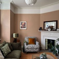 Plaster pink living room with a grey and white patterned armchair, white picture rail and moss green sofa.