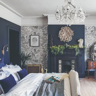 Navy blue and grey bedroom with block navy walls and grey wallpaper, including fireplace, prints and bed