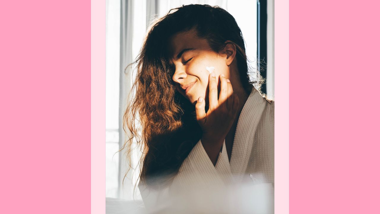 woman applying sunscreen on pink background