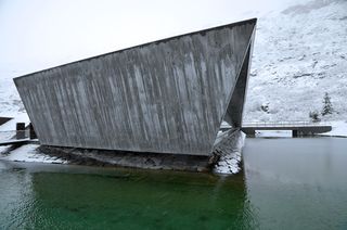 Close up view of the Trollstigen Visitor Centre's concrete exterior. The building is surrounded by water and a snow covered landscape