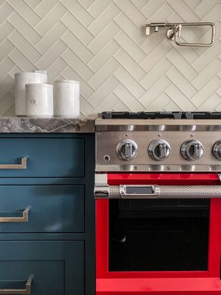A kitchen with dark green cabinets and a bright red oven