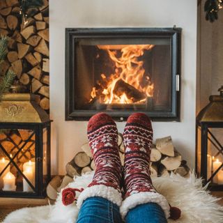 A person relaxing their feet by the fire while wearing a pair of red and white Christmas patterned fluffy socks.