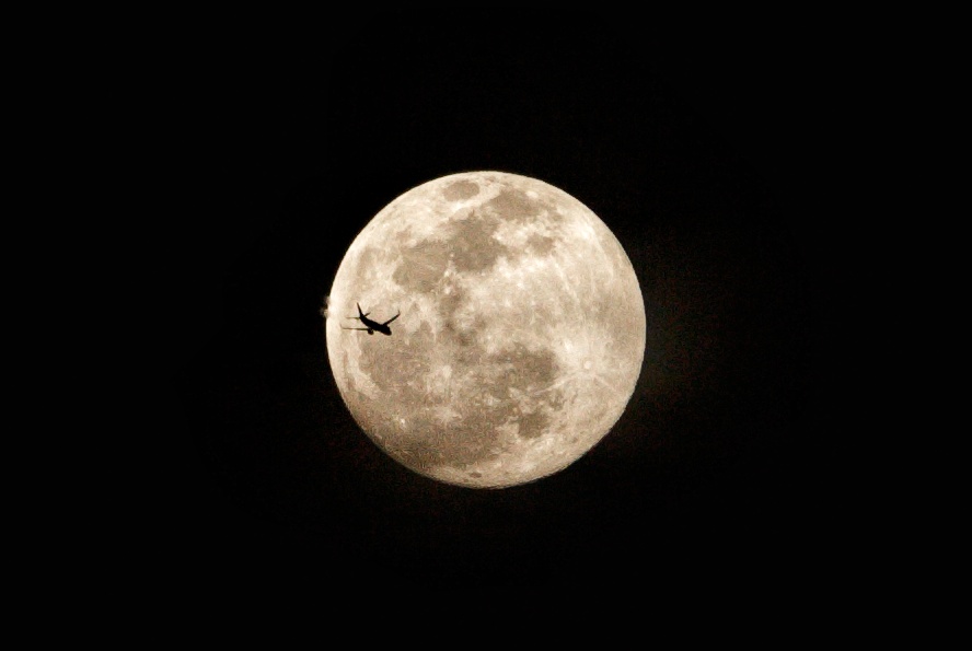 A photograph of a plane flying in front of the Harvest supermoon.