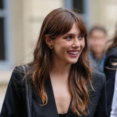 a white woman with dark hair and bangs being photographed by paparazzi