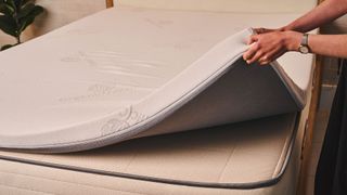 A hand lifts up the 3" Latex Mattress Topper by Brooklyn Bedding to see if it needs replacing