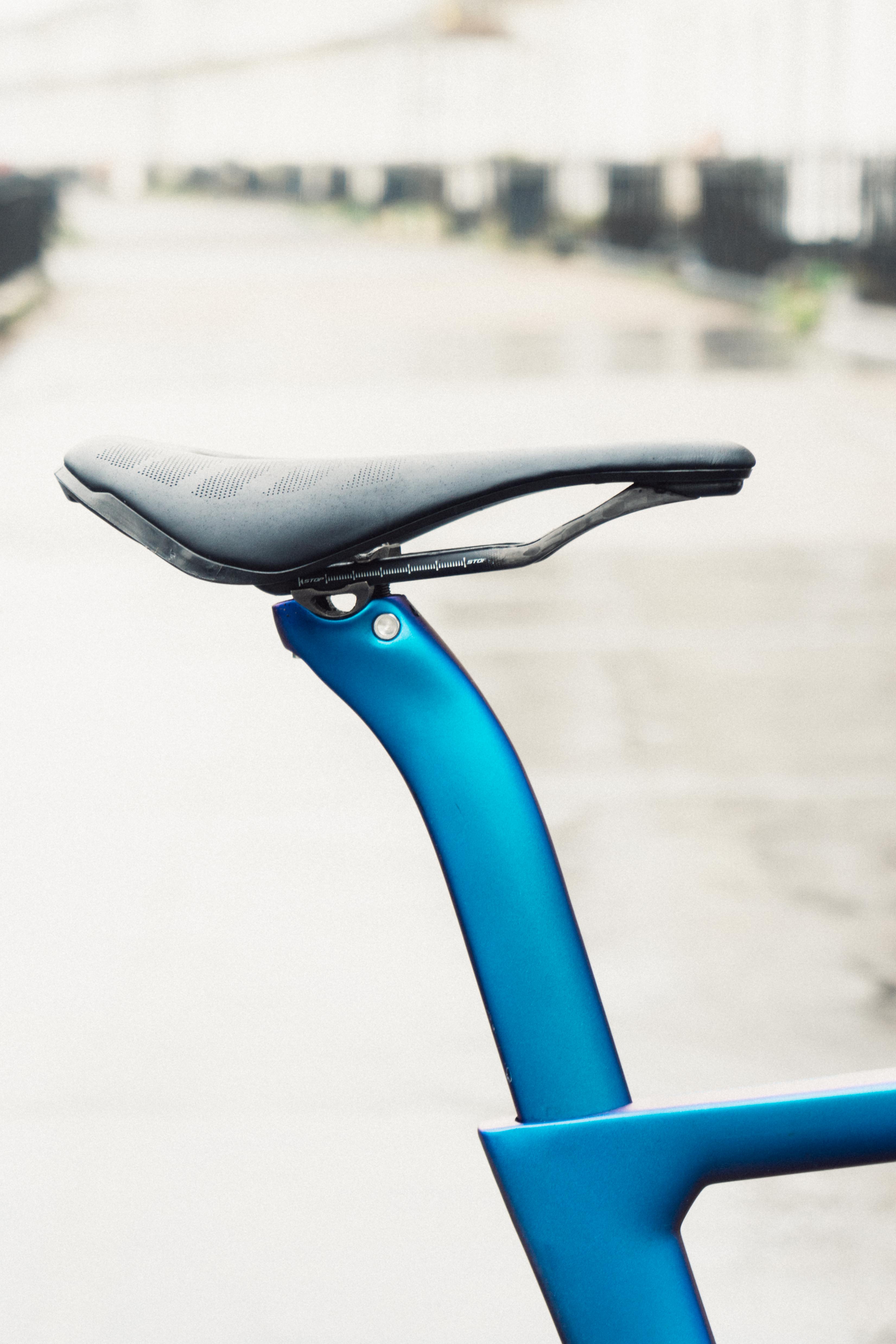 A close up of a blue seatpost with a saddle pushed right forwards