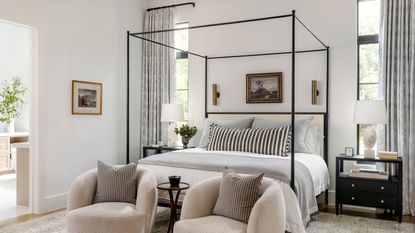 cozy bedroom with four poster bed, striped lumbar pillow, two boucle armchairs at the foot of the bed