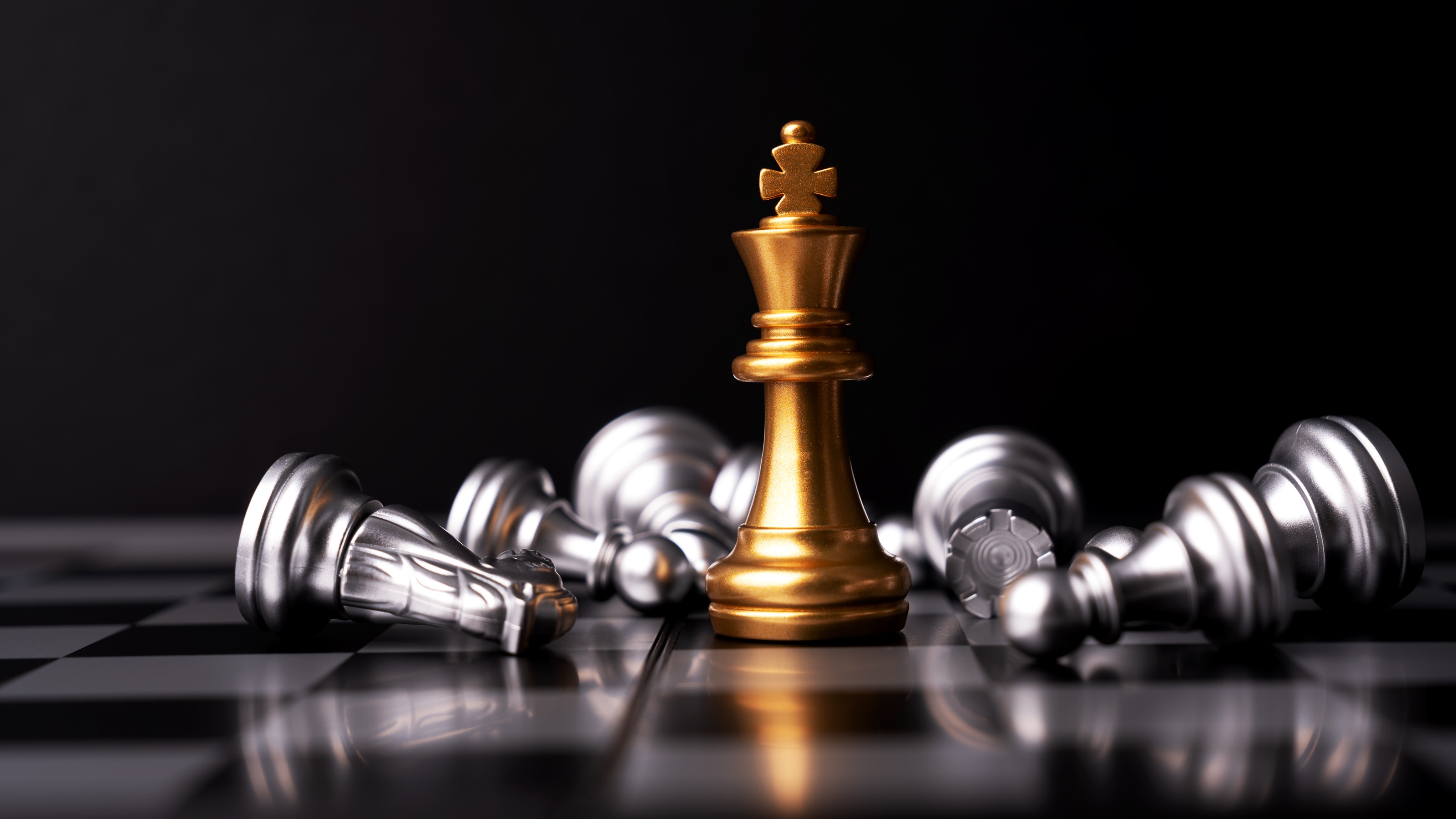A gold king on a chessboard is surrounded by fallen chess pieces in silver.