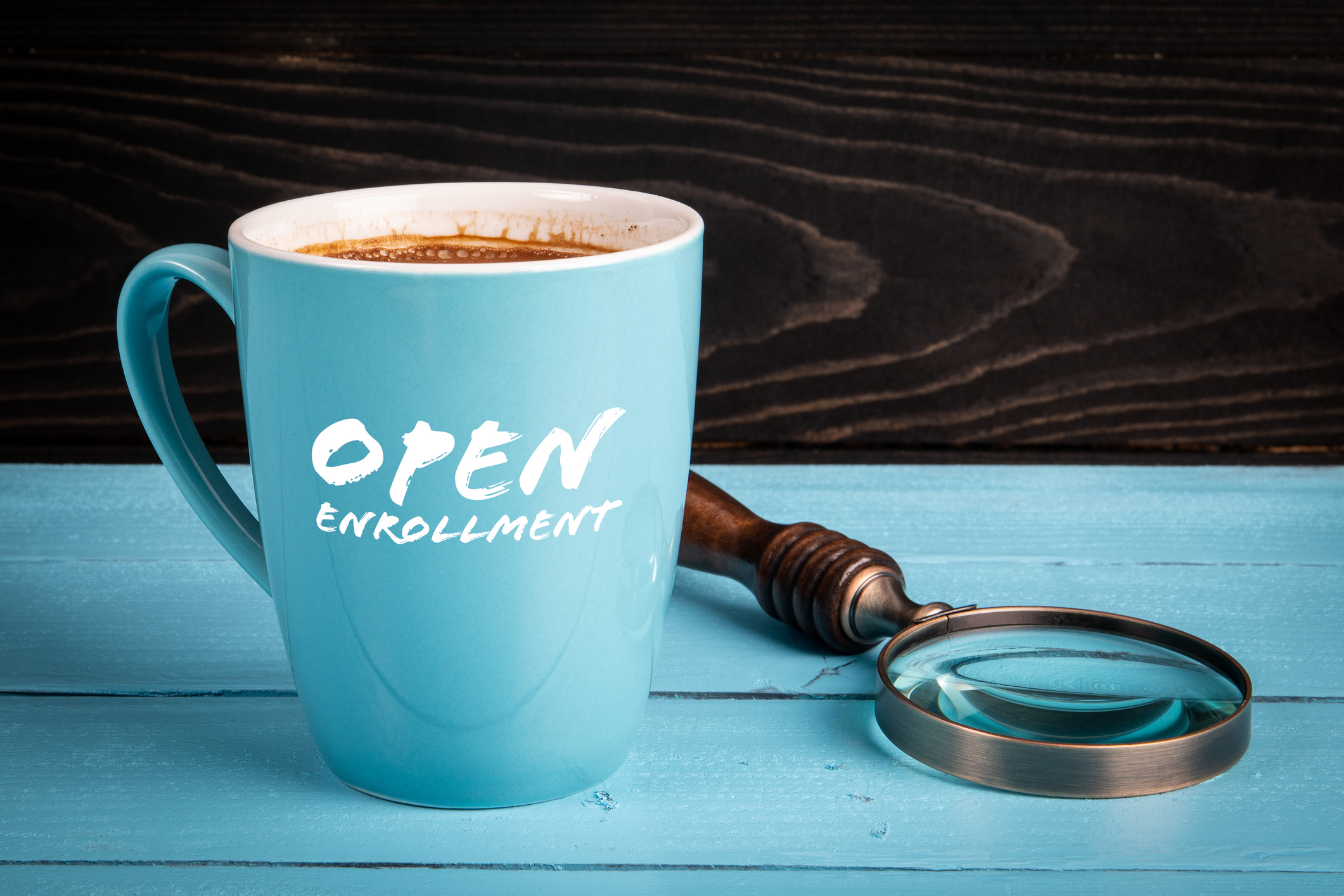 coffee cup with the words open enrollment on it on a table next to a magnifying glass