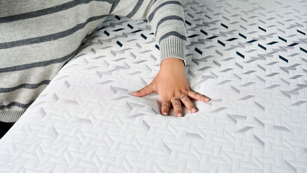 A woman's hand resting on the surface of the Nectar Ultra Hybrid mattress showing how the soft material gives way