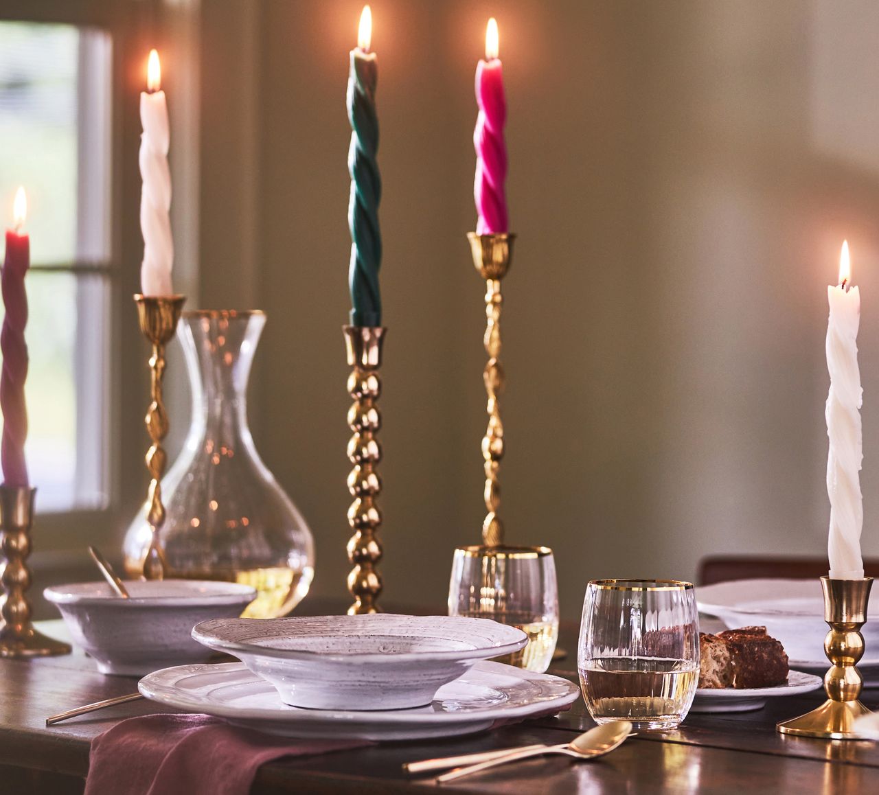 Colorful taper candles in gold holders surround a luxurious place setting at a table.