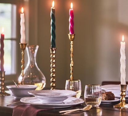 Colorful taper candles in gold holders surround a luxurious place setting at a table.