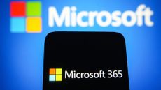 Microsoft 365 logo and branding pictured on a smartphone screen with Microsoft logo and branding pictured in background.