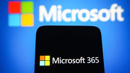 Microsoft 365 logo and branding pictured on a smartphone screen with Microsoft logo and branding pictured in background.