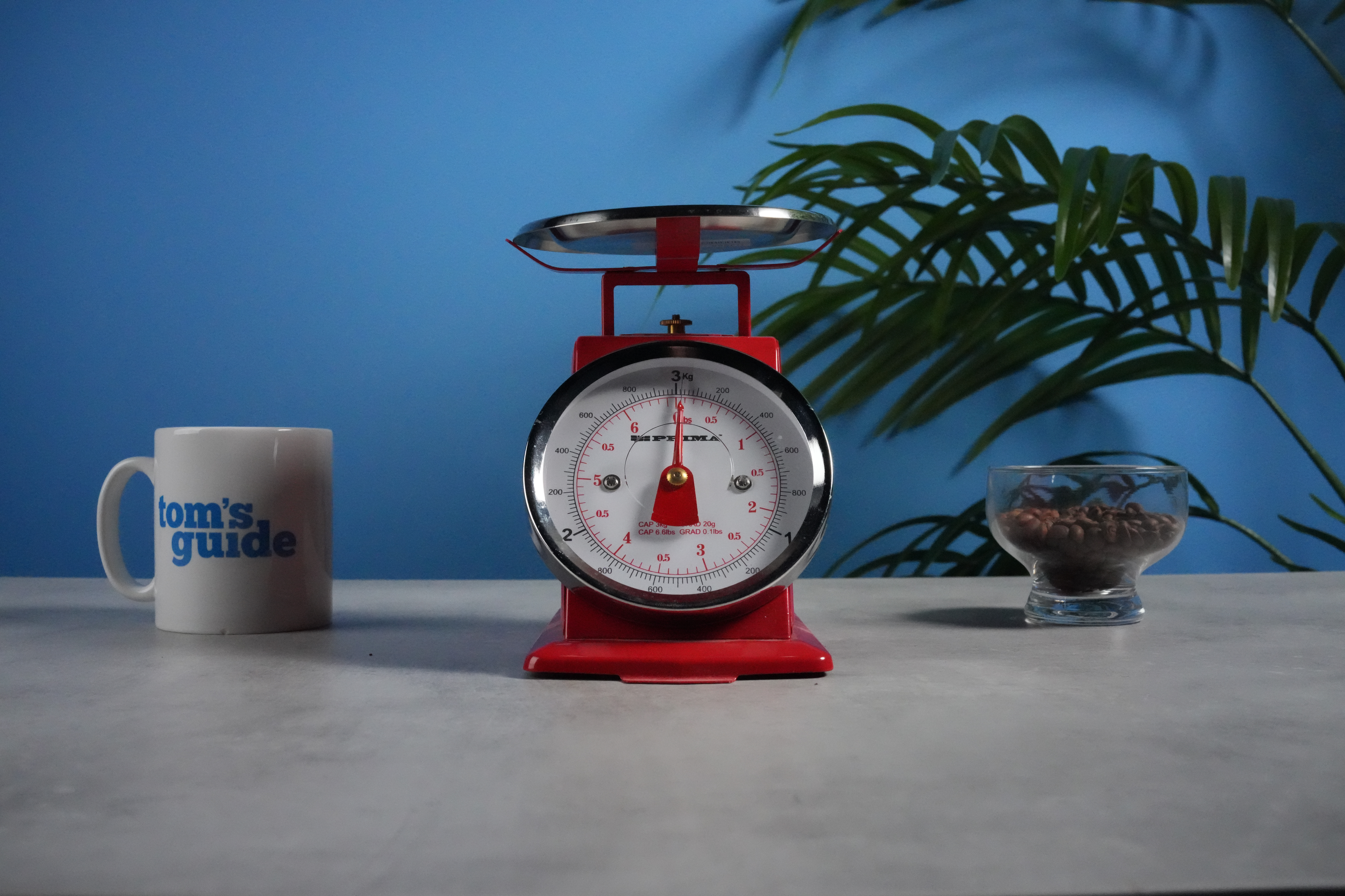 A photo of a set of red scales next to a Tom's Guide mug and some coffee beans, with a blue wall in the background
