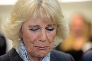 Queen Camilla wearing a blue scarf and looking down crying during a meeting with the mother of a domestic abuse victim