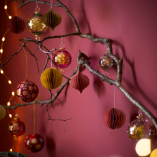 Red and golden Christmas baubles on branch in front of red wall.