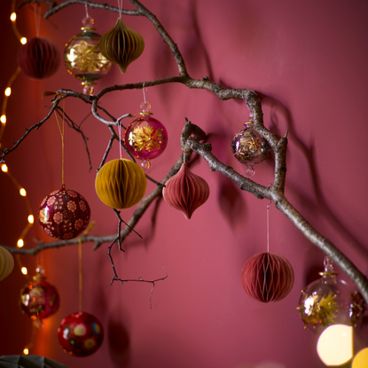 Red and golden Christmas baubles on branch in front of red wall.