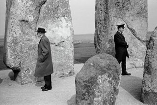 Two official looking men staring in opposite directions at Stonehenge