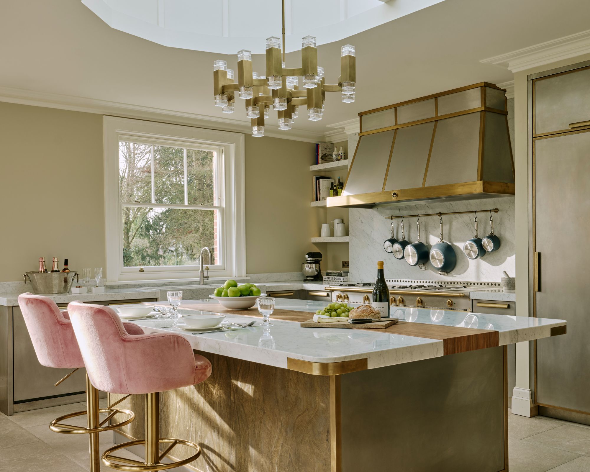 A gold kitchen with marble and wood accents with pink stools