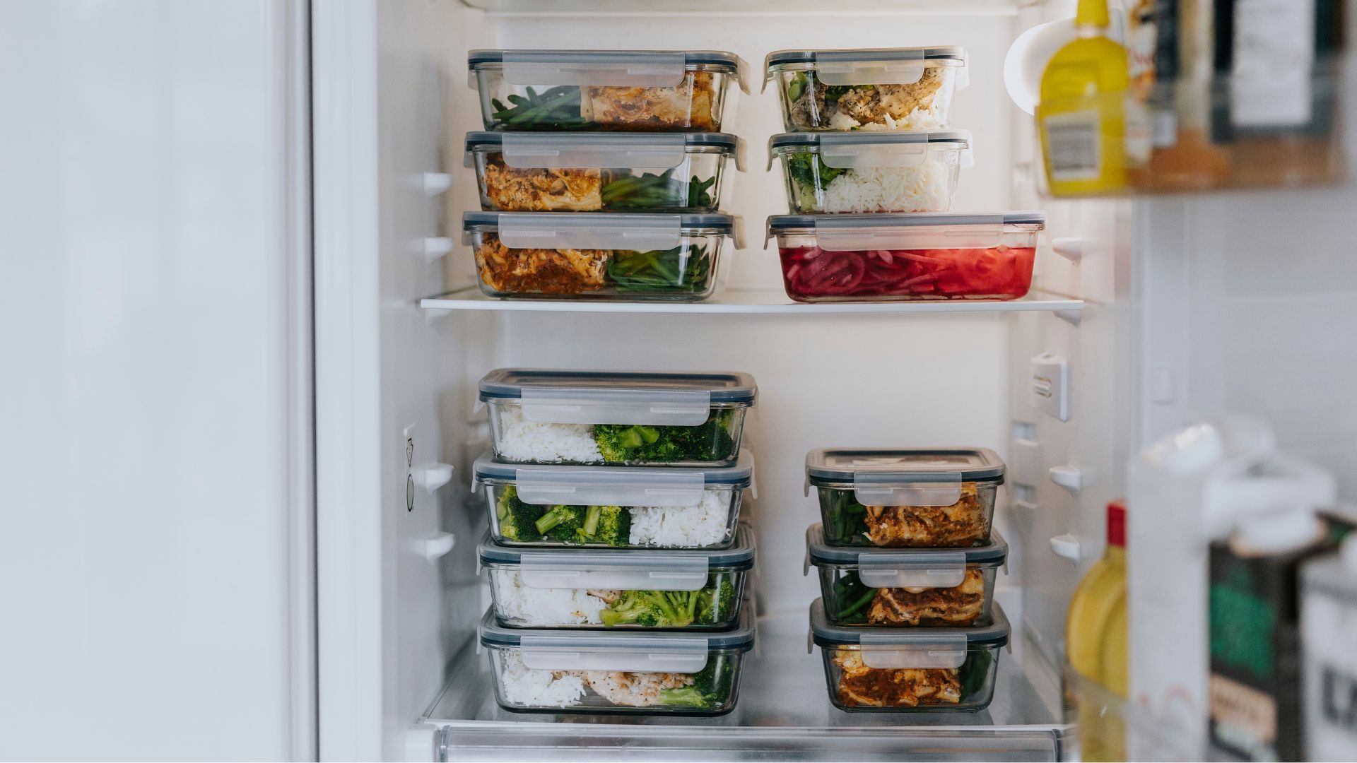 Glass tupperware inside an open fridge showing food storage