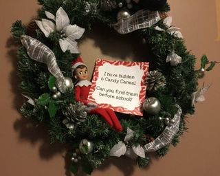 An elf figurine on a Christmas wreath with candy cane treasure hunt signage
