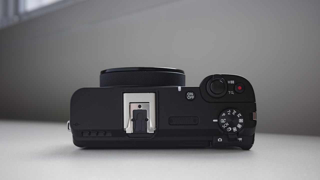 Top plate of the Canon PowerShot V1 compact vlogging camera on a white desk, lens retracted