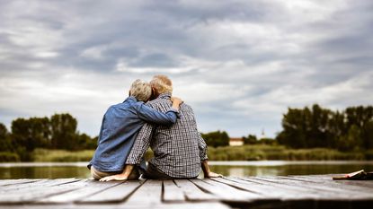 A retired couple sit together on a dock.