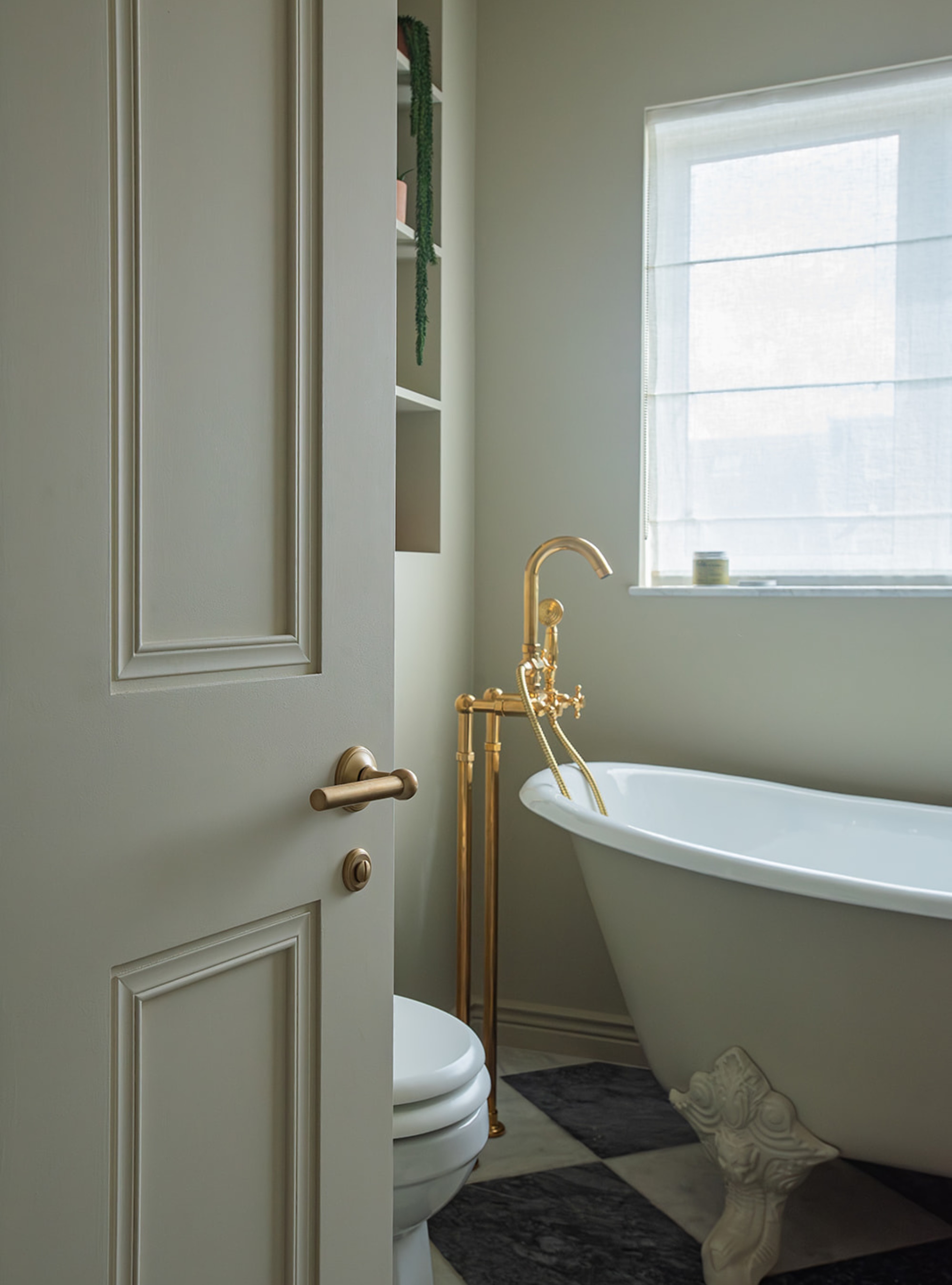 sage green color drenched bathroom in Bone by Farrow &amp;amp; Ball with freestanding painted tub, brass freestanding tap, checkerboard floors, voile roman blinds over window