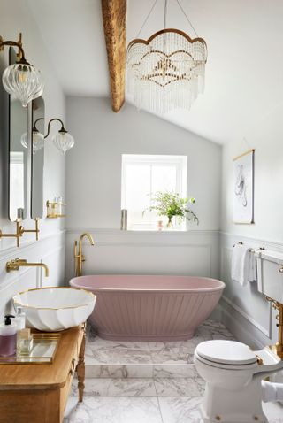 A small bathroom with marble flooring and a pink bath with a vertical ribbed design