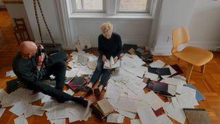 Meyerowitz and Barret say on a wooden floor surrounded by papers of writing, Meyerowitz looking through his rangefinder camera at Barrett