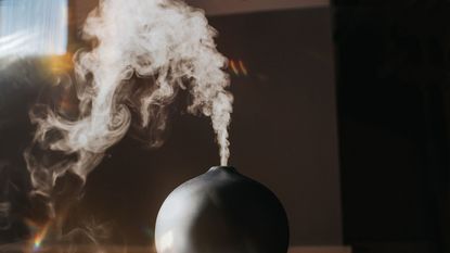 A black humidifier turned on with a puff of white vapor above it 